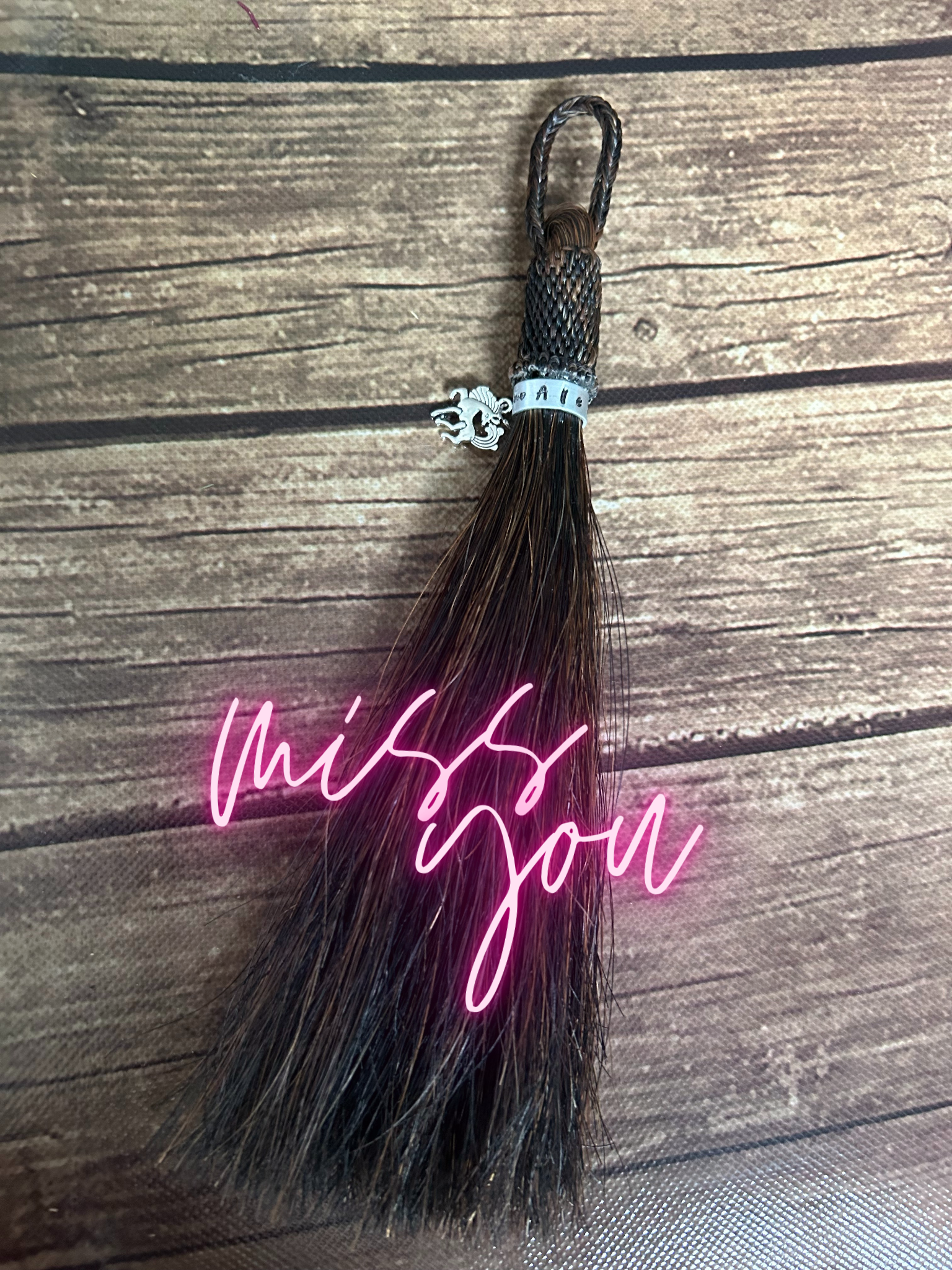 Horse hair tassel with a metal name tag and horse charm.  The words "Miss you" are overlaid in neon pink.